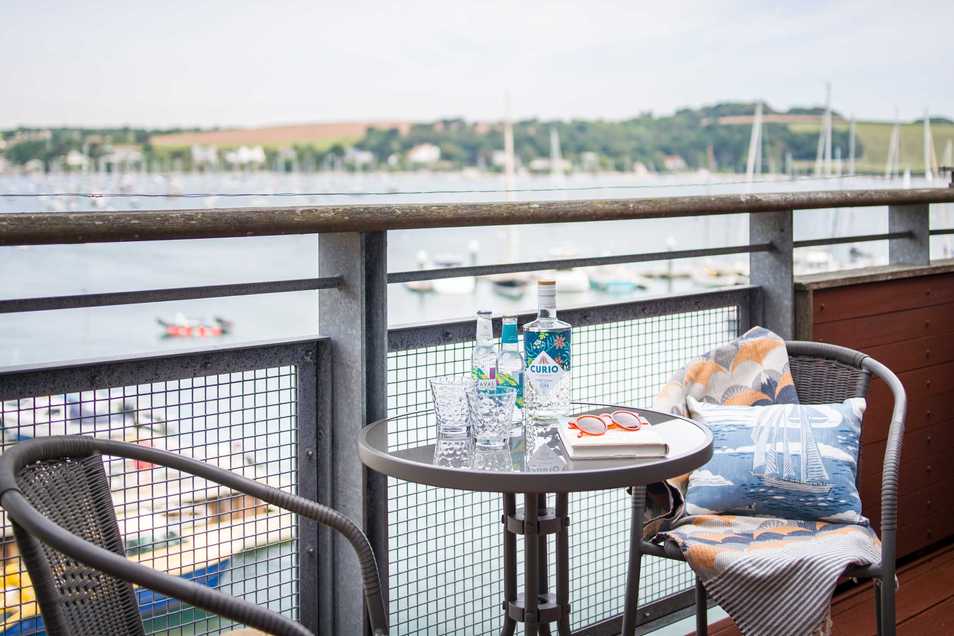 Balcony of Seacape with a view out over Falmouth Harbour. Two chairs are beside a round table laid out for a G&T.